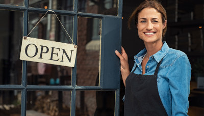 woman standing in front of store holding open sign